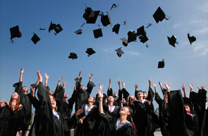 newly graduated people wearing black academy gowns throwing hats up in the air