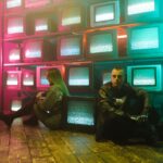 man and woman sitting on the floor beside televisions